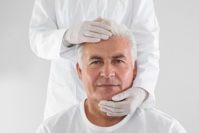 Photo of Doctor examining senior man face before cosmetic surgery on white background