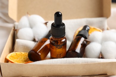 Bottles of organic cosmetic products, dried orange slices and cotton flowers in box, closeup