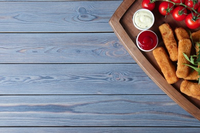 Photo of Board with cheese sticks, sauces and tomatoes on table, top view. Space for text