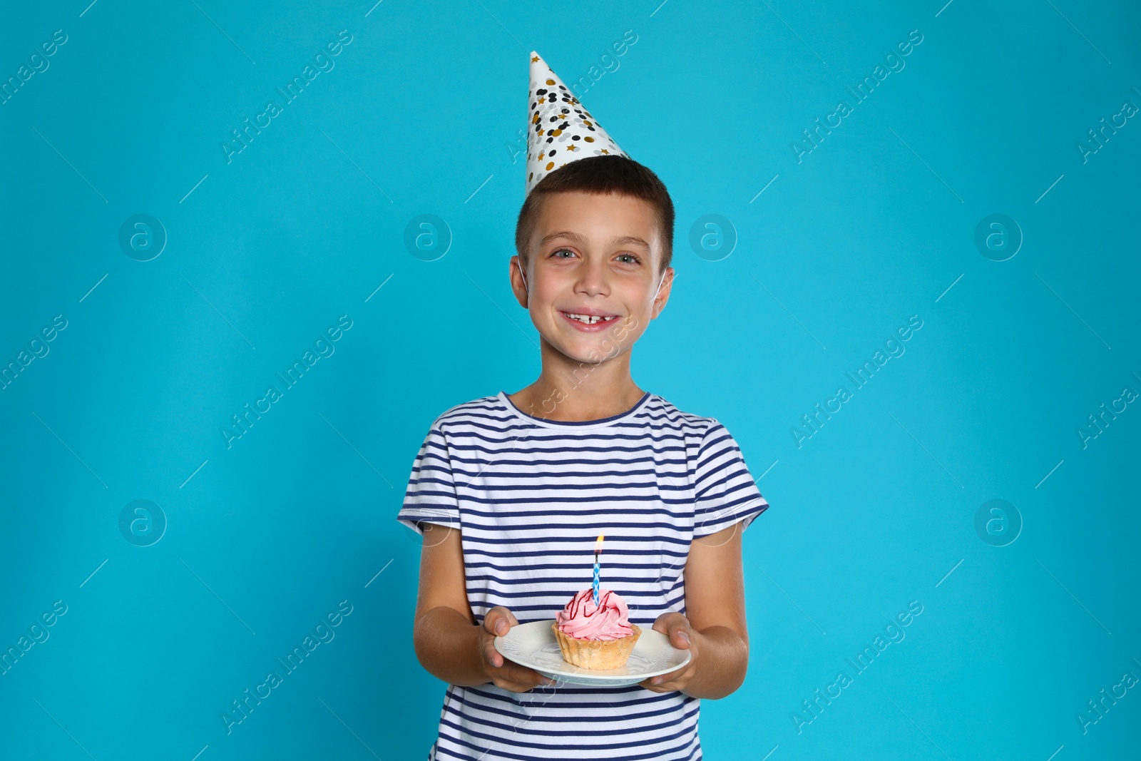 Photo of Happy boy holding birthday cupcake with candle on blue background