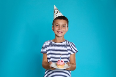 Happy boy holding birthday cupcake with candle on blue background