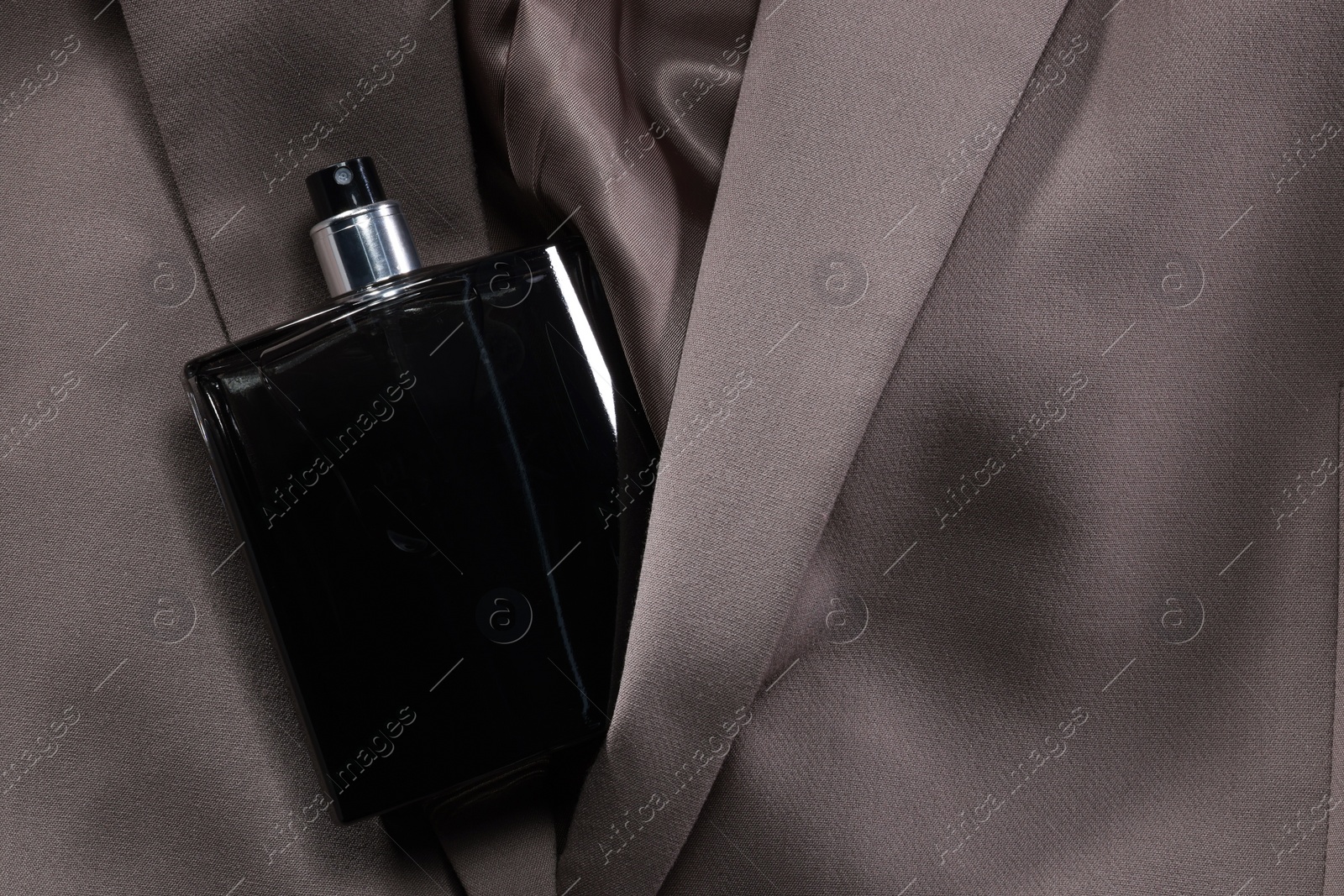 Photo of Luxury men's perfume in bottle on beige jacket, top view. Space for text
