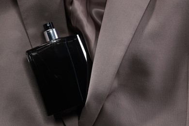 Luxury men's perfume in bottle on beige jacket, top view. Space for text