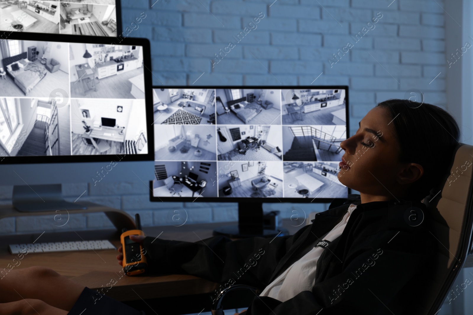 Photo of Female security guard sleeping near monitors at workplace