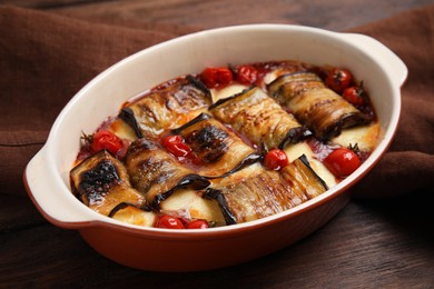Photo of Tasty eggplant rolls with tomatoes and cheese in baking dish on wooden table, closeup