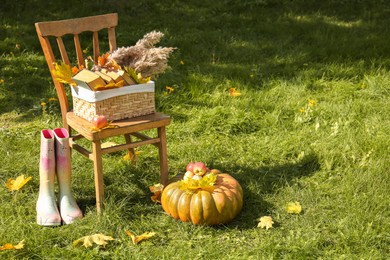 Photo of Rubber boots, chair, pumpkin and apples on green grass, space for text. Autumn atmosphere