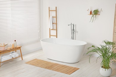 Photo of Stylish bathroom interior with ceramic tub and houseplants