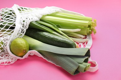 Photo of String bag with different vegetables on bright pink background, closeup