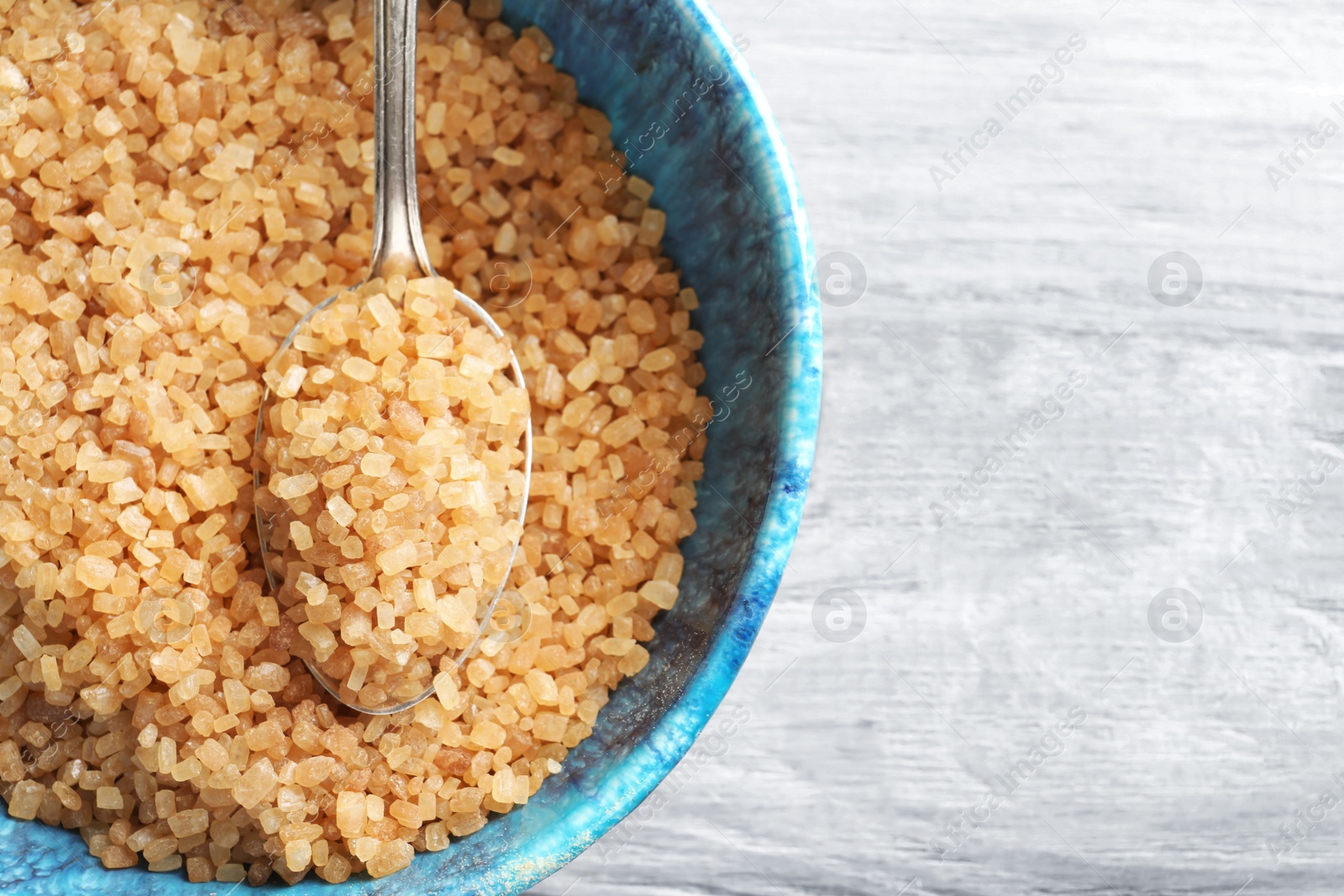 Photo of Spoon with brown sugar in bowl on table, closeup