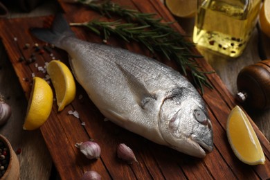 Photo of Raw dorado fish, lemon wedges and spices on wooden table