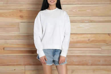 Photo of Young woman in sweater at wooden wall, closeup. Mock up for design