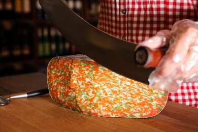 Photo of Seller cutting delicious cheese on table in store