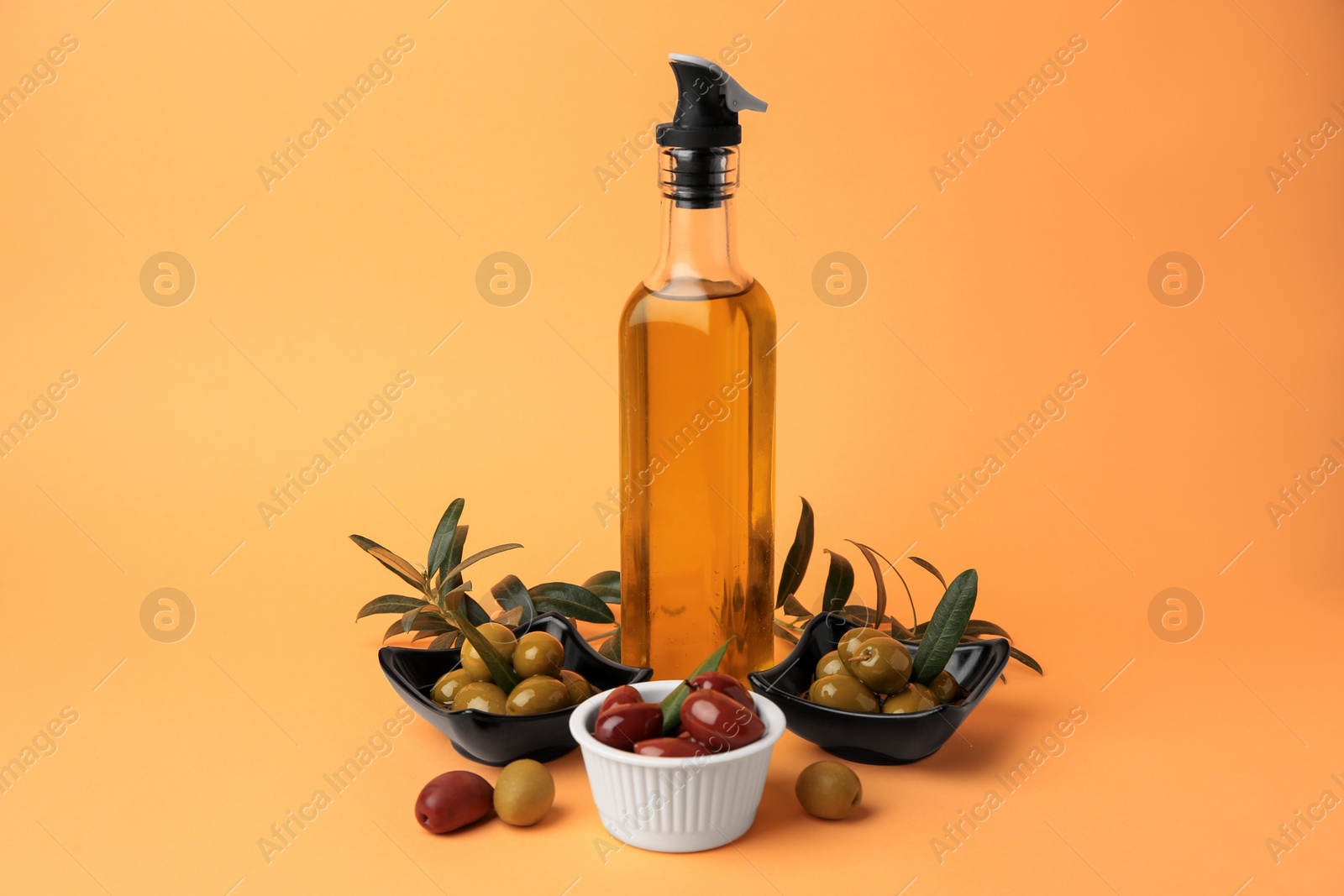 Photo of Bottle of oil, olives and tree twigs on orange background