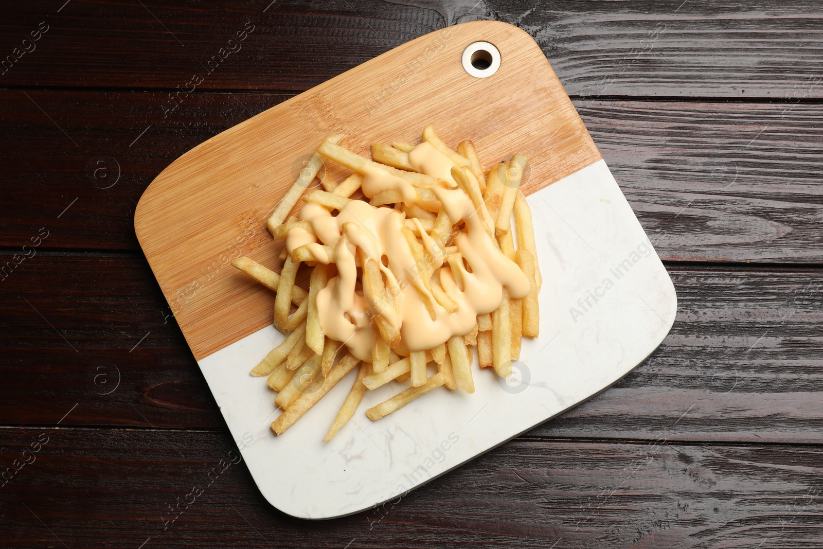 Photo of Delicious french fries with cheese sauce on wooden table, top view