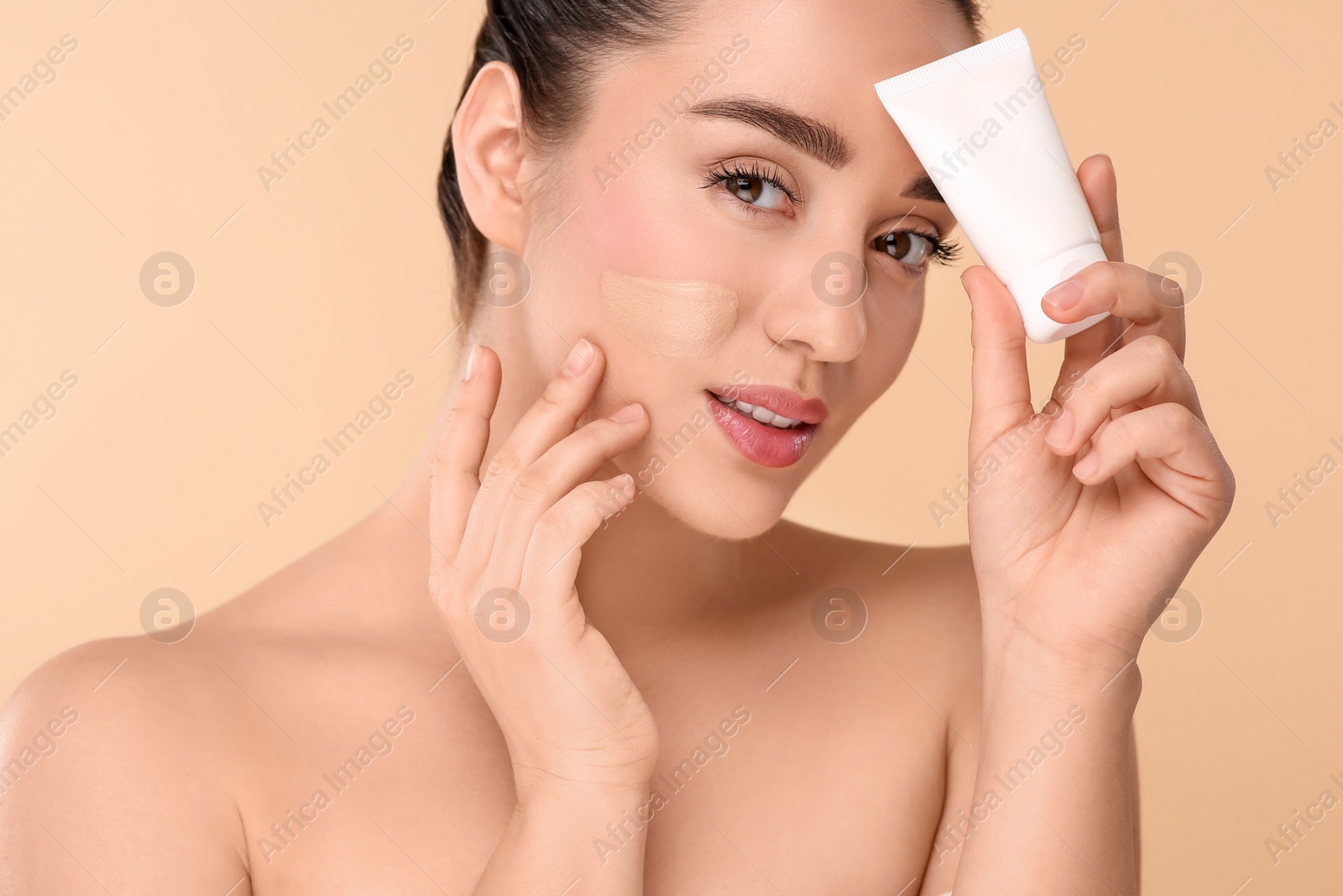 Photo of Woman holding tube of foundation on beige background