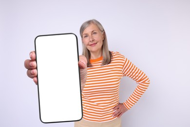 Happy mature woman showing mobile phone with blank screen on white background. Mockup for design