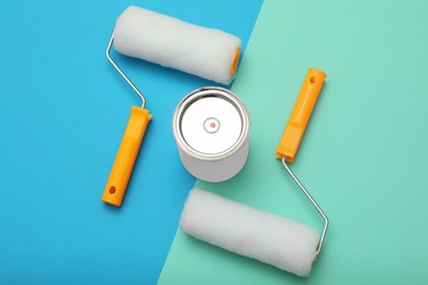 Photo of Can of orange paint and roller brushes on color background, flat lay