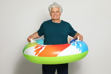 Photo of Funny mature man with bright inflatable ring on light background