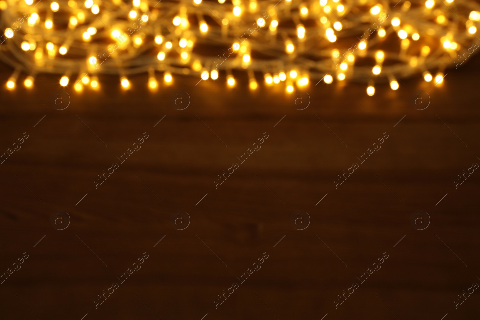 Photo of Blurred view of glowing Christmas lights on wooden table, space for text