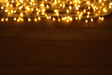 Blurred view of glowing Christmas lights on wooden table, space for text