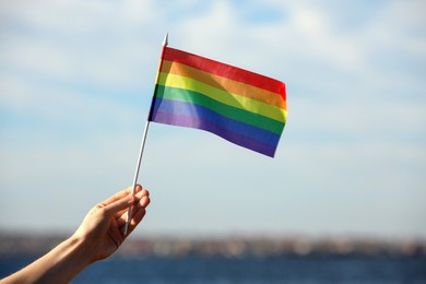 Photo of Woman holding bright LGBT flag near river, closeup