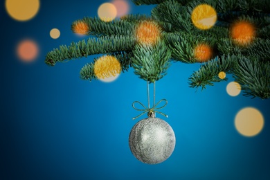 Beautiful Christmas ball hanging on fir tree branch against light blue background, bokeh effect