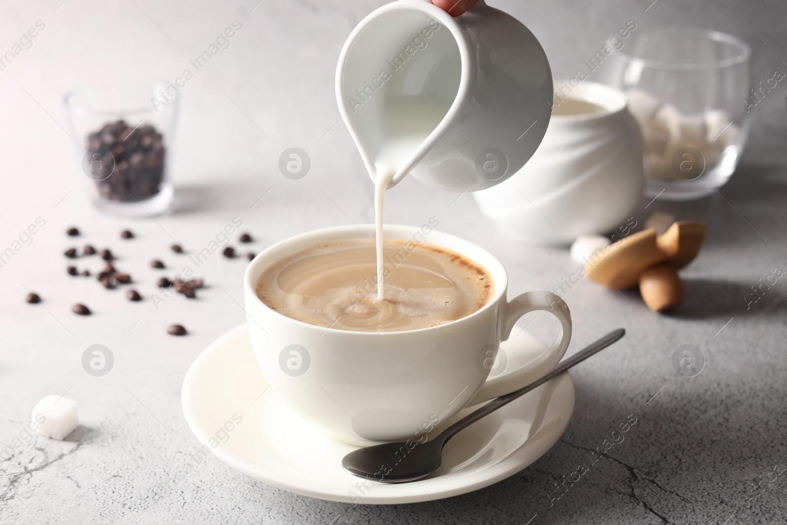 Photo of Pouring milk into cup with coffee on light grey textured table, closeup