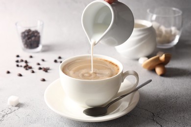 Photo of Pouring milk into cup with coffee on light grey textured table, closeup