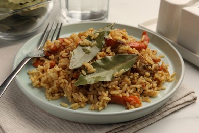 Delicious pilaf, bay leaves and fork on white table