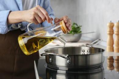 Vegetable fats. Woman pouring cooking oil into frying pan on stove in kitchen, closeup