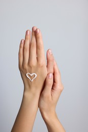 Photo of Heart painted with cream on hand against light grey background, closeup
