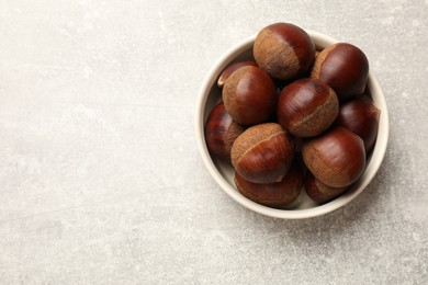 Roasted edible sweet chestnuts in bowl on light grey table, top view. Space for text