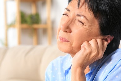 Photo of Senior woman suffering from ear pain at home, closeup. Space for text