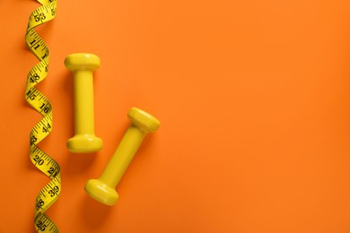 Dumbbells and measuring tape on orange background, flat lay with space for text. Weight loss concept