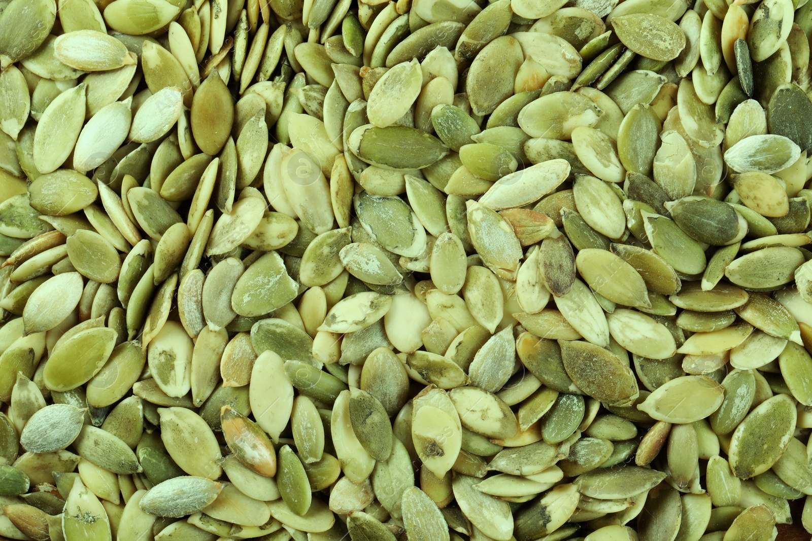 Photo of Many peeled pumpkin seeds as background, top view