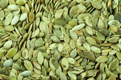 Photo of Many peeled pumpkin seeds as background, top view