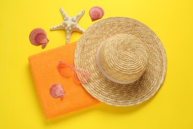 Beach towel, straw hat and sunglasses on yellow background, flat lay