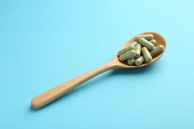 Photo of Vitamin capsules in wooden spoon on light blue background