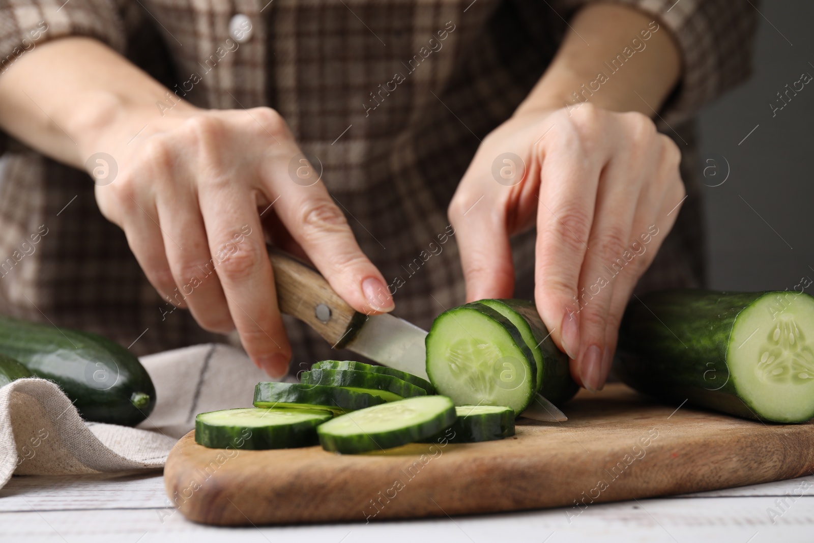 Photo of Woman cutting fresh cucumber at white wooden table, closeup