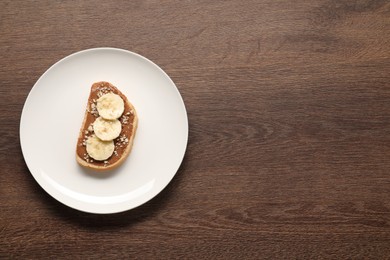 Photo of Toast with peanut butter, banana slices and nuts on wooden table, top view. Space for text