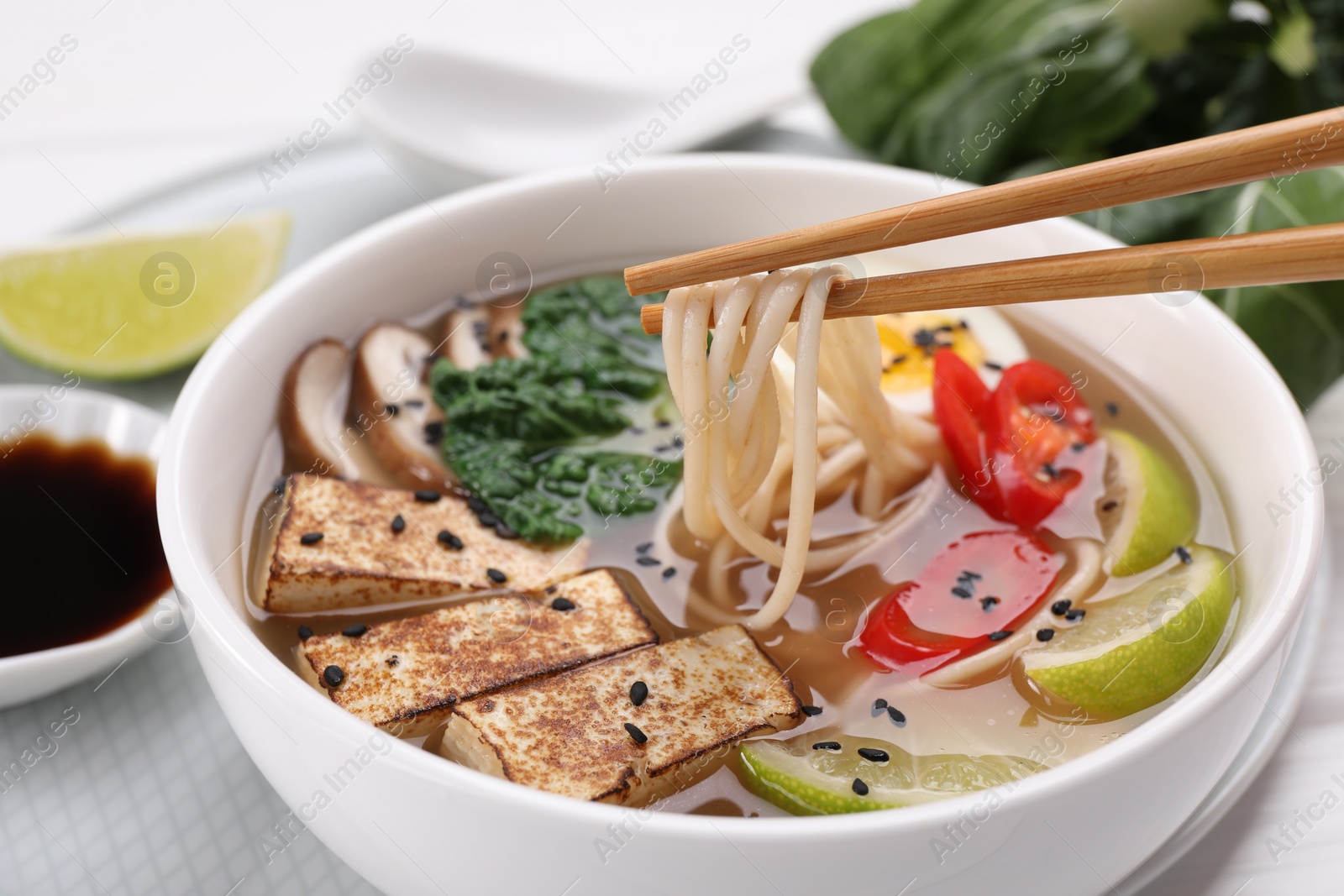 Photo of Eating delicious vegetarian ramen with chopsticks at table, closeup