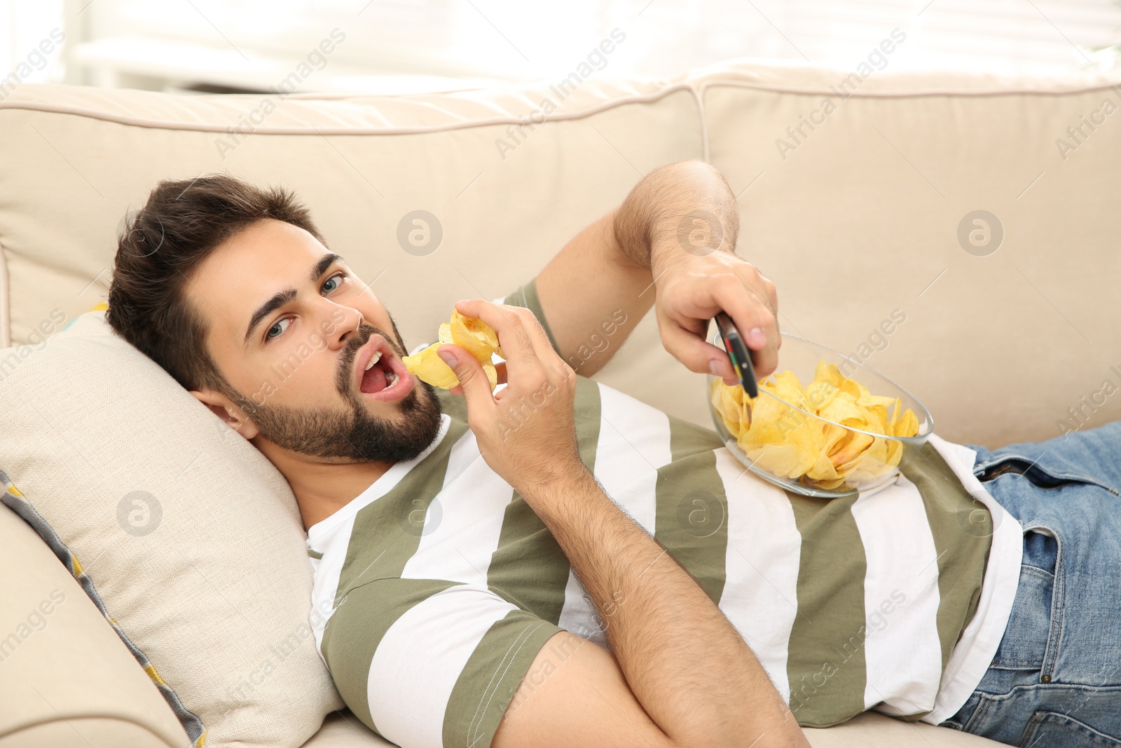 Photo of Lazy young man with potato chips watching TV on sofa at home