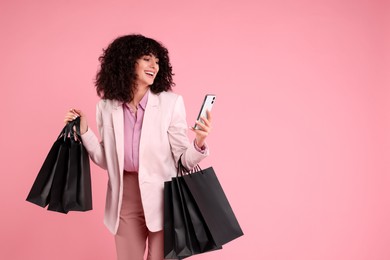 Photo of Happy young woman with shopping bags and modern smartphone on pink background. Space for text