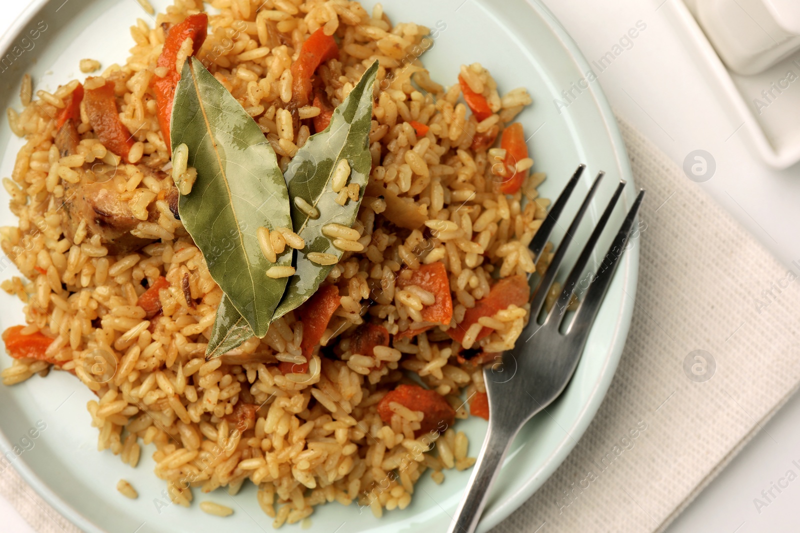 Photo of Delicious pilaf, bay leaves and fork on table, top view