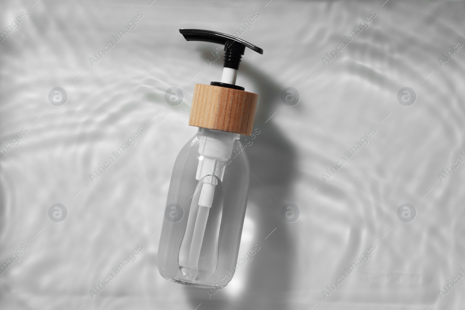 Photo of Bottle of cosmetic product in water on white background, top view. Space for text