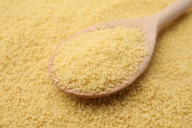 Photo of Wooden spoon and uncooked organic couscous as background, closeup