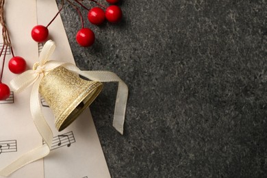 Photo of Golden shiny bell with white bow, decorative berries and music sheets on grey textured table, flat lay and space for text. Christmas decoration