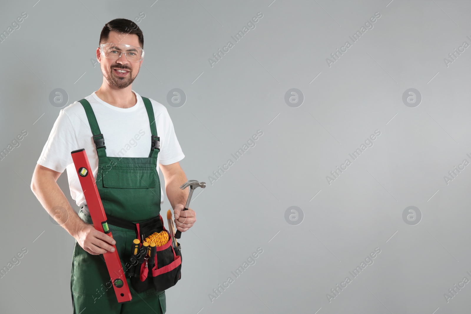 Photo of Portrait of professional construction worker with tools on grey background, space for text