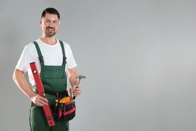 Photo of Portrait of professional construction worker with tools on grey background, space for text