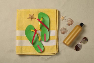 Beach towel, flip flops, sunscreen, sunglasses, starfishes and seashells on sand, flat lay